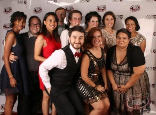 Digital Media staff and students pose against a logo patterned backdrop. 